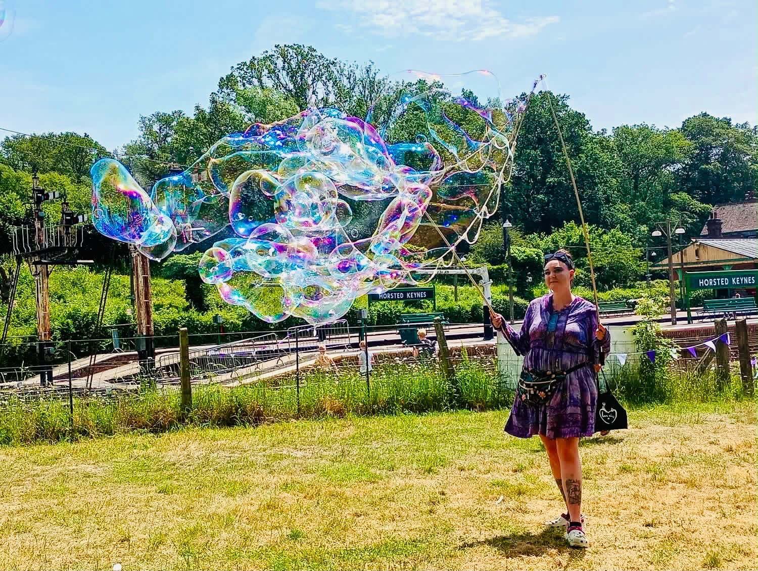 A performer making giant bubbles for a child in a sunny outdoor garden