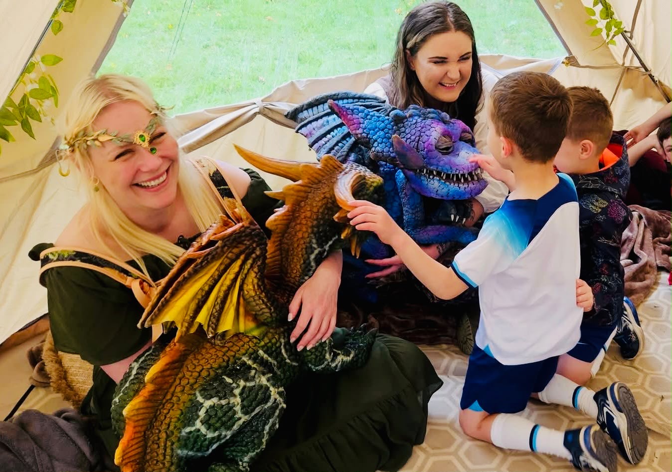 A child meeting a green dragon with two costumed handlers inside a bell tent
