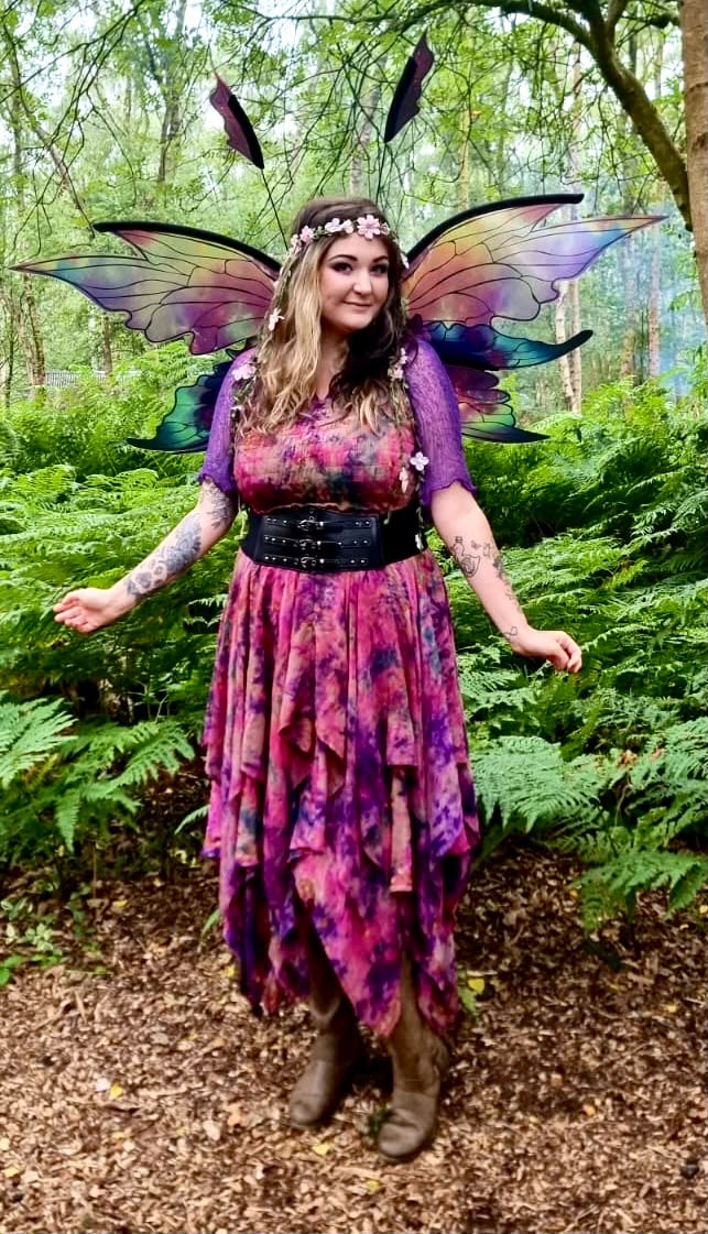 A winged fairy in a purple dress standing on a woodland path