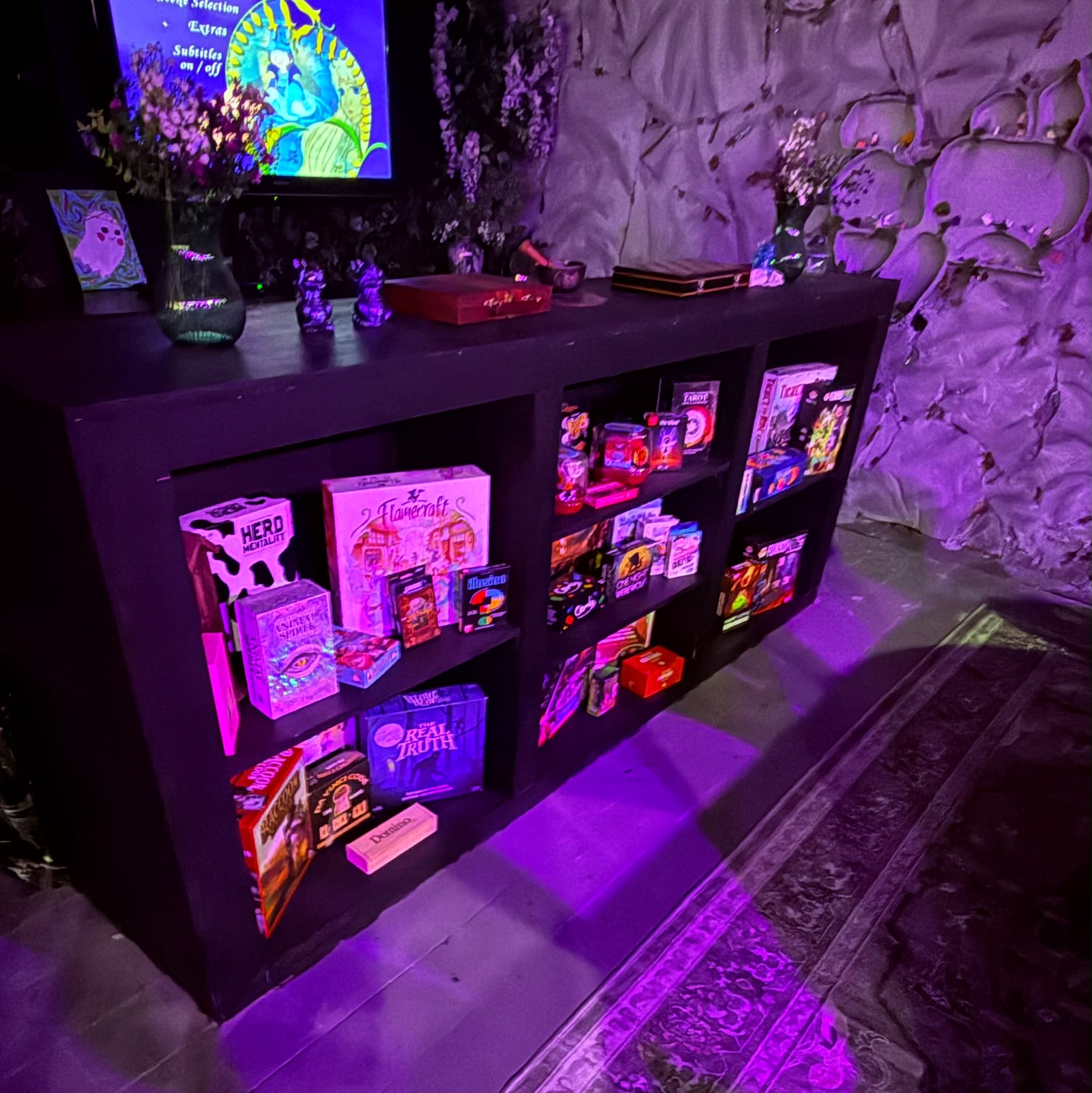 A shelf of board games beneath a screen and purple lighting in the Gaming Lair