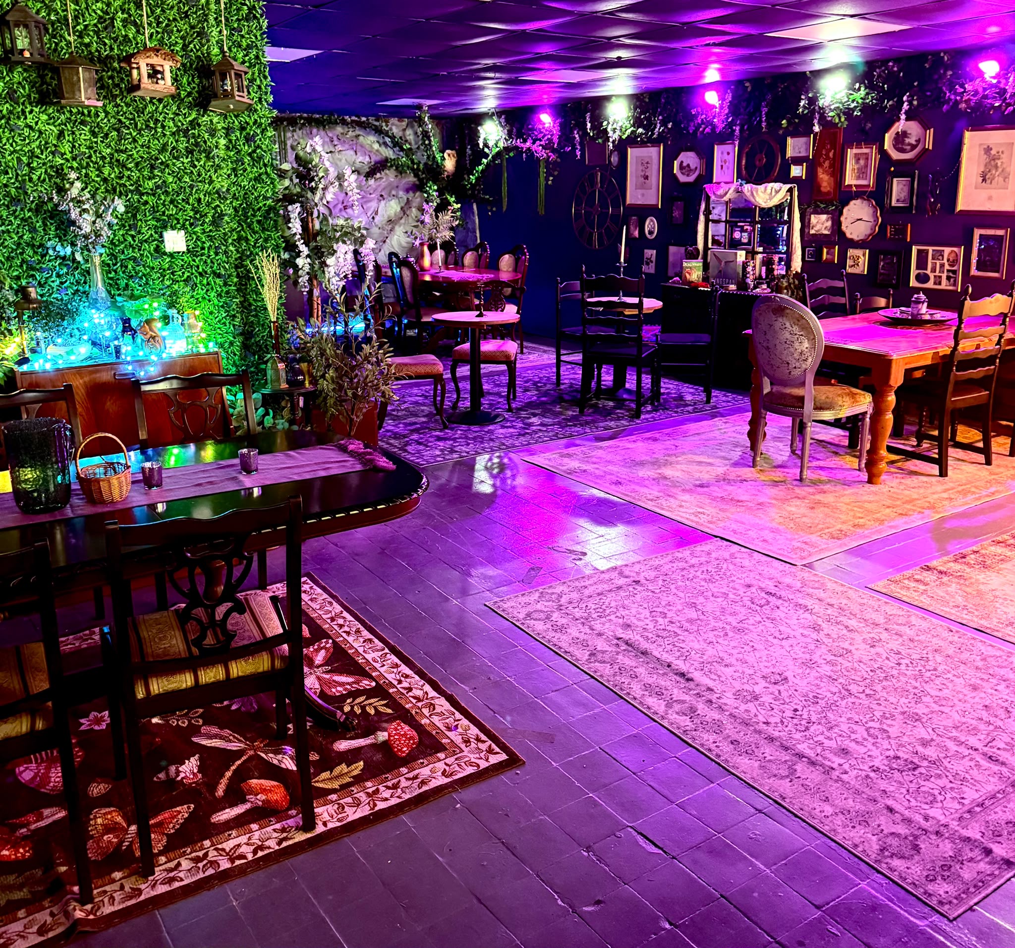 Tables, vintage chairs and lanterns in the venue beneath purple lighting and leafy walls