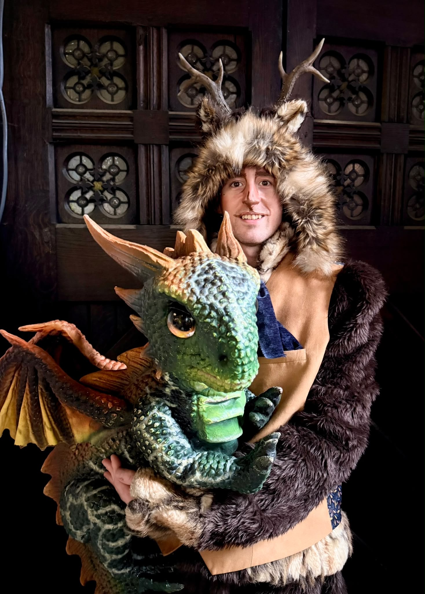 An antlered woodland character holding a green dragon puppet
