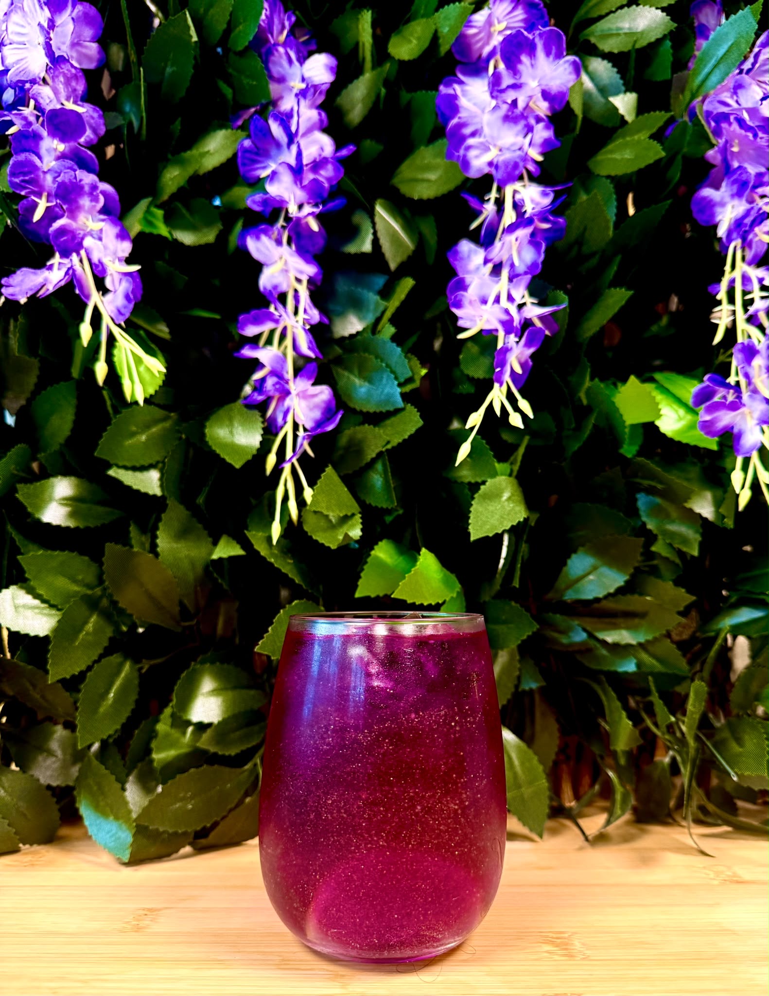A purple drink on a wooden table beneath trailing wisteria