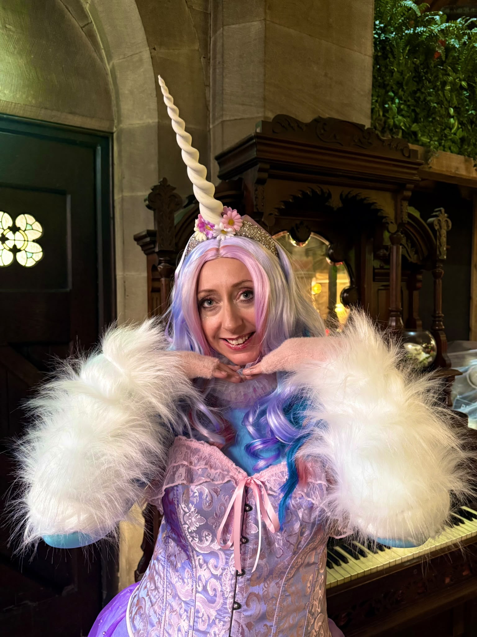 A smiling unicorn character in a purple dress with fluffy white sleeves