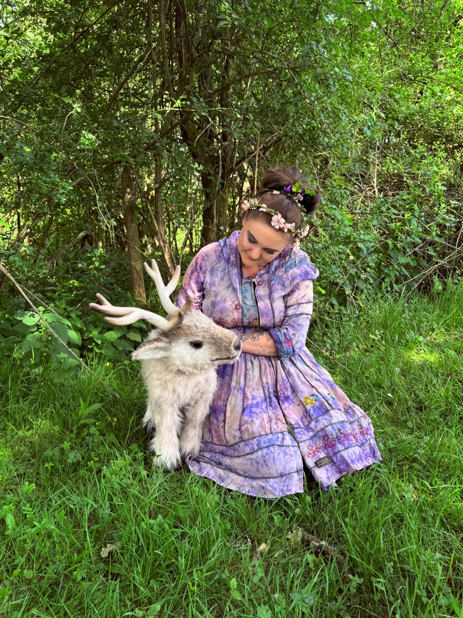 A storyteller kneeling beside a reindeer puppet in a woodland glade